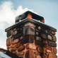Rustic Stone Chimney Emitting Smoke Against a Cloudy Blue Sky in Wintertime Landscape